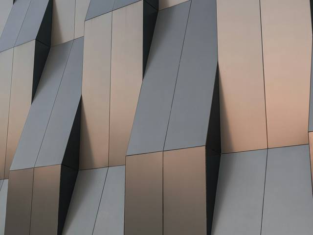 La imagen muestra una pared con un diseño arquitectónico contemporáneo que presenta ángulos y formas geométricas en tonos metálicos.