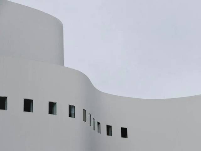 La imagen muestra una estructura arquitectónica moderna con formas curvas y colores claros en un entorno nublado.