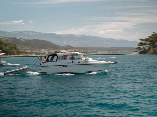 Un barco navega por aguas tranquilas con un paisaje montañoso al fondo.