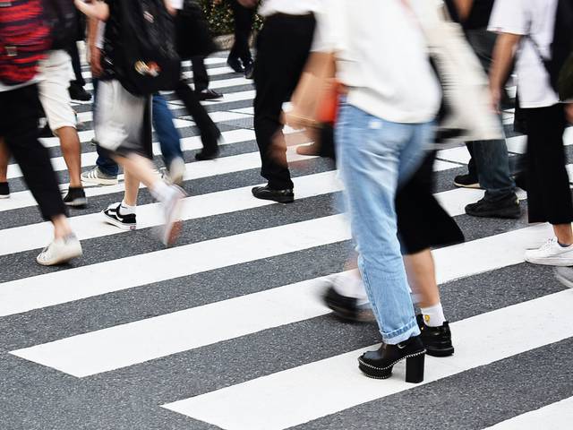 Una multitud de personas cruza una calle con rayas blancas y negras.