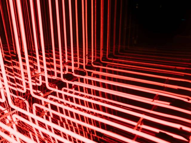 La imagen muestra un conjunto de tubos fluorescentes iluminados en color rojo formando una estructura geométrica.