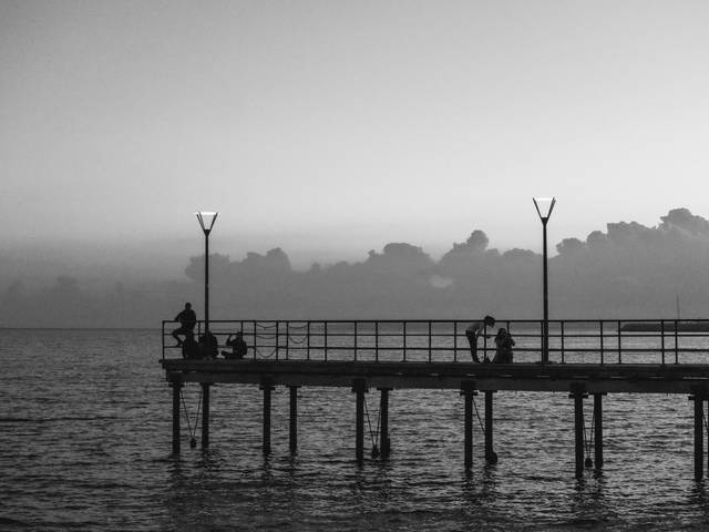 Una pareja se sienta en un muelle al atardecer, contemplando el mar y el cielo nublado.