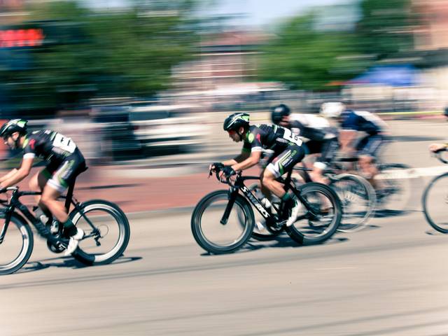 Un grupo de ciclistas compite en una carrera, mostrando velocidad y dinamismo en un entorno urbano.