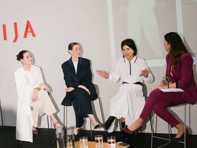 Un grupo de mujeres vestidas elegantemente participa en una conversación en un evento.