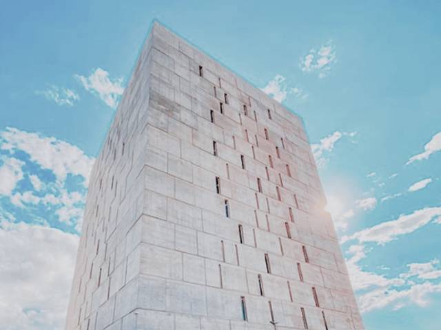 Una torre de concreto se eleva bajo un cielo azul salpicado de nubes.