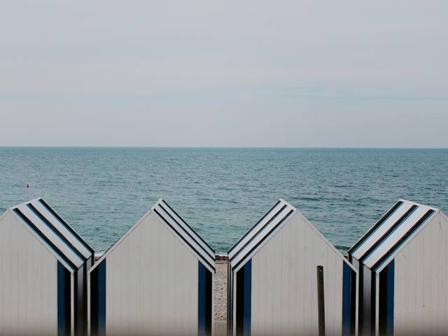 La imagen muestra una fila de cabañas de playa con el mar de fondo bajo un cielo nublado.