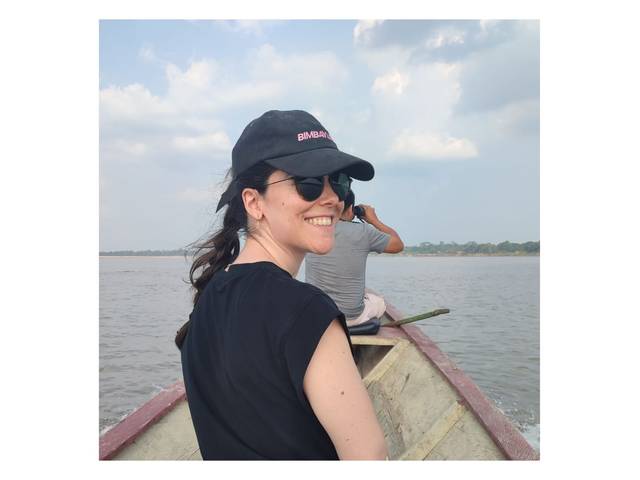 Una mujer sonriente lleva una gorra y gafas de sol mientras está en una canoa, en un paisaje acuático.
