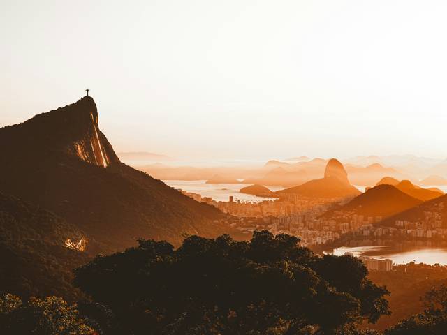 Una vista panorámica de montañas y una ciudad al atardecer con un cielo anaranjado.