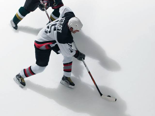 Dos jugadores de hockey sobre hielo compiten por el puck en una pista de hielo.