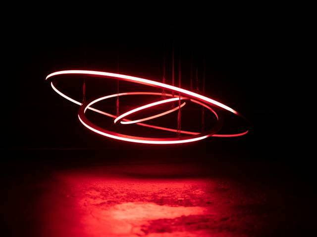 Una escultura moderna iluminada por luces rojas en un fondo oscuro.
