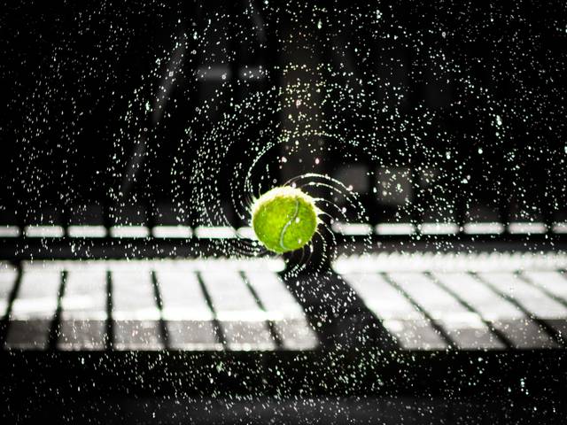 Una pelota de tenis verde rebota en un entorno húmedo, creando un efecto visual de agua salpicando a su alrededor.