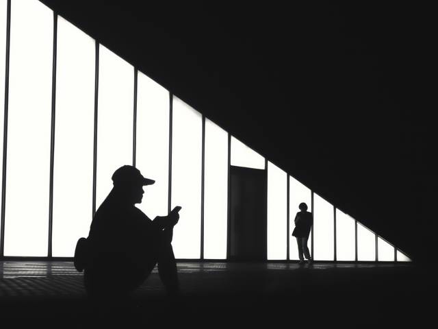 Siluetas de personas en un espacio arquitectónico iluminado por grandes ventanales.