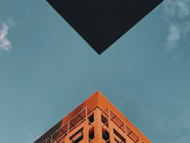 Una construcción moderna resalta bajo un cielo azul, con un gran objeto cuadrado negro flotando encima.