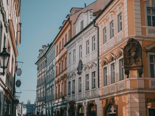 Una calle con edificios históricos de arquitectura europea en tonos claros bajo un cielo azul.