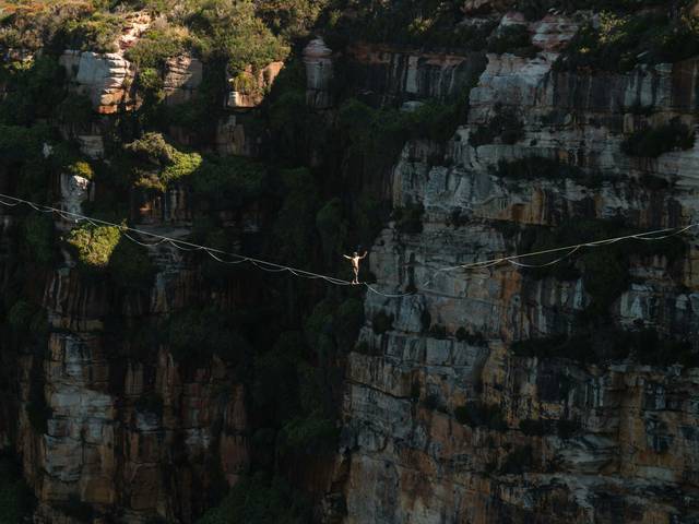 Una persona camina sobre una cuerda floja entre altos acantilados rocosos.
