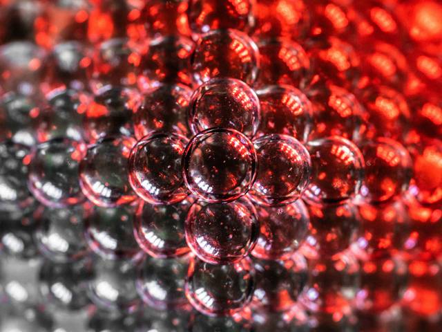 La imagen muestra una multitud de esferas brillantes en tonos rojos y grises, creando un efecto visual interesante.