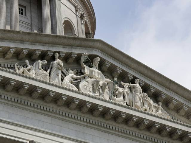 Parte superior de un edificio con esculturas en relieve que representan figuras alegóricas.