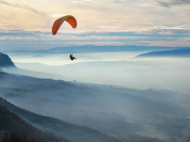 Un parapentista vuela sobre un paisaje montañoso cubierto de niebla al amanecer.