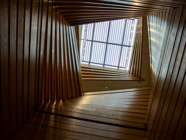 La imagen muestra una vista desde el interior de un edificio con una estructura de madera en espiral y una ventana en la parte superior.