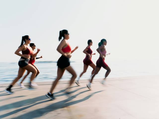 Un grupo de mujeres corriendo junto a la orilla del mar en un día soleado.
