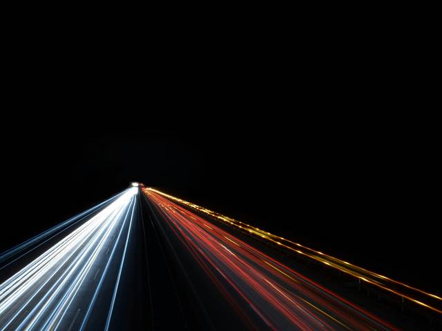 Una carretera iluminada con luces de vehículos en movimiento contra un fondo oscuro.