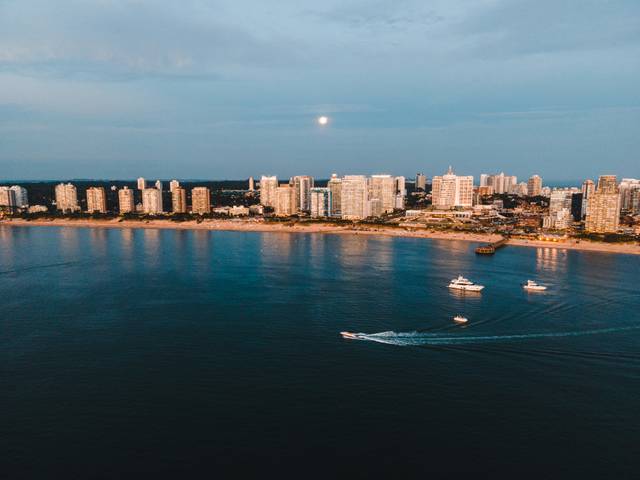 Vista aérea de una ciudad costera al atardecer con edificios y barcos en el agua.