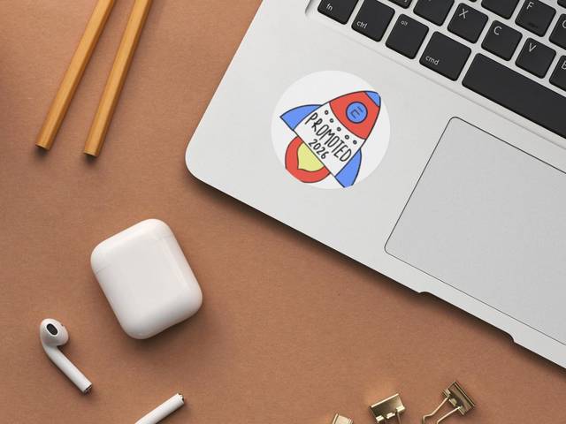 Una laptop sobre una superficie marrón con un adhesivo de cohete y auriculares.
