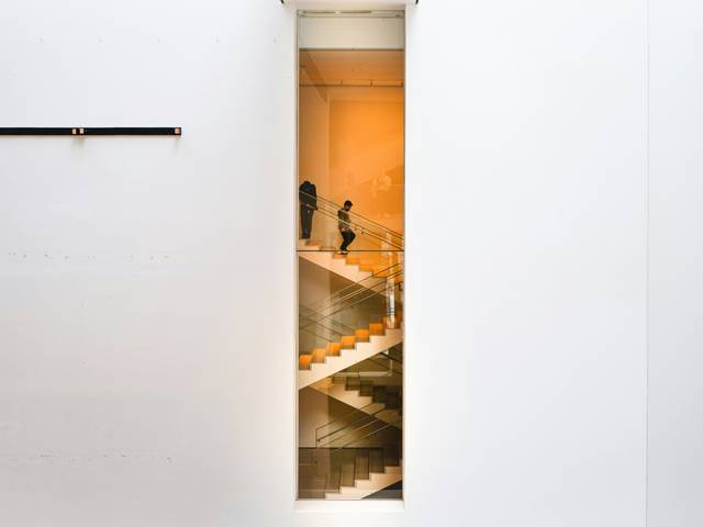 Una imagen que muestra un espacio arquitectónico moderno con escaleras en el fondo y paredes blancas predominantes.