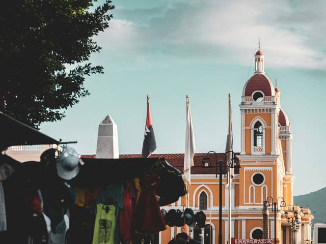 Una vista de un edificio amarillo con cúpulas rojas y banderas, en un entorno urbano.
