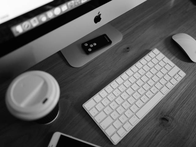 Una vista aérea de una mesa de trabajo con un ordenador, un teclado, un ratón, un teléfono móvil y un vaso de café.