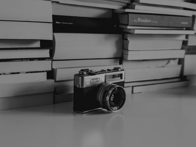 Una cámara antigua está situada sobre una superficie blanca, rodeada de libros apilados.