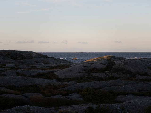 Una vista tranquila de un barco navegando en el horizonte sobre un mar sereno al atardecer.