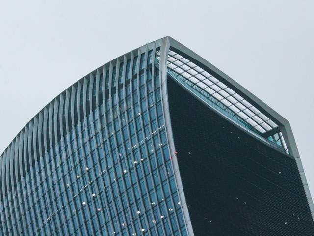 Imagen de la parte superior de un moderno edificio de cristal con forma curvada.