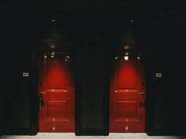 Dos puertas rojas iluminadas en un pasillo oscuro.