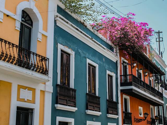 Una colorida calle con edificios de diferentes tonalidades y plantas en los balcones.
