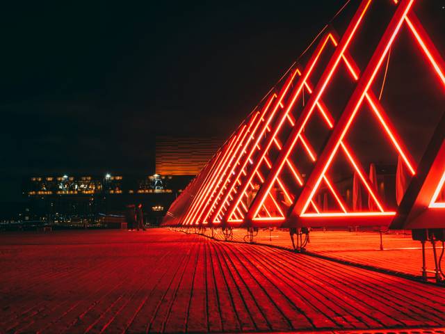 Una serie de estructuras en forma de triángulo iluminadas con luces rojas en un entorno nocturno.