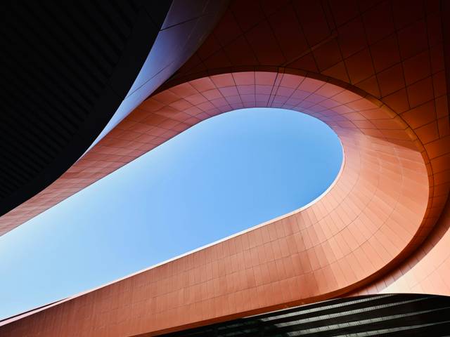Una vista arquitectónica que muestra una estructura con formas curvilíneas y un cielo azul en el fondo.