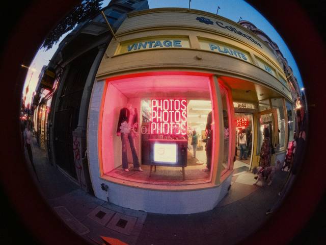 Una tienda vintage con un escaparate iluminado en tonos rosados que muestra el texto 'PHOTOS'.