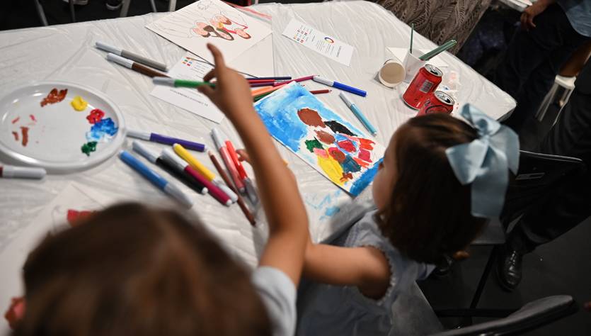 Un grupo de niños está pintando en una mesa con diversas obras de arte y materiales de dibujo a su alrededor.