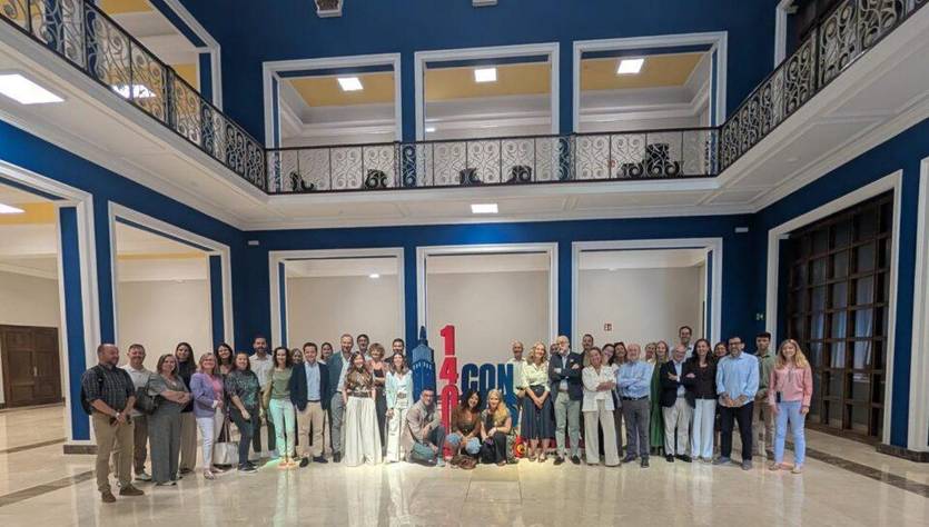 Un grupo de personas posando en un edificio con un fondo azul y letras que dicen '14CON'.