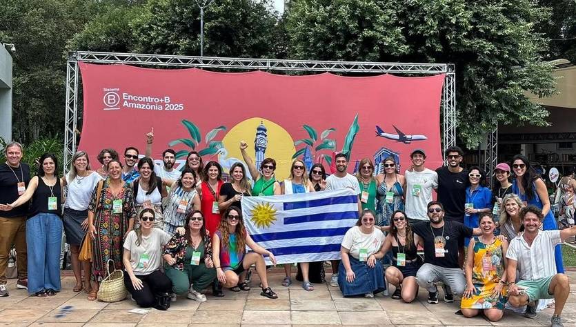 Un grupo de personas sonrientes posando frente a un telón decorativo con símbolos de Uruguay y el logotipo de un evento.