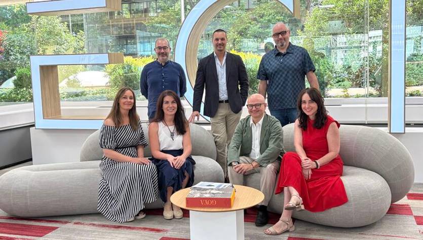 Un grupo de personas posan en un ambiente moderno y luminoso, sentados en sofás suaves frente a un gran letrero.