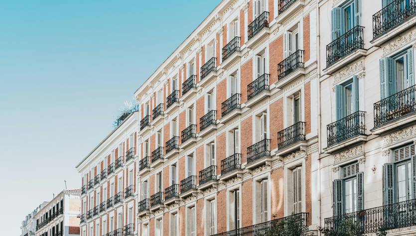 Una imagen de edificios en una calle de la ciudad con balcones y un cielo despejado.
