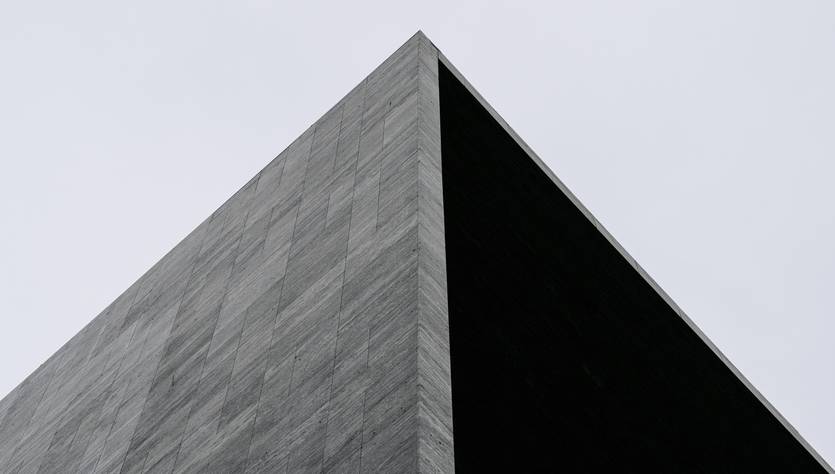 Una estructura arquitectónica con un diseño angular y materiales oscuros que se eleva contra un cielo nublado.