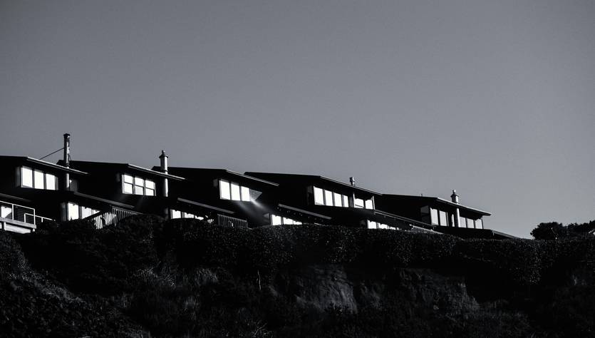 Una fila de casas oscuras se alza sobre un acantilado, iluminadas por la luz del sol.