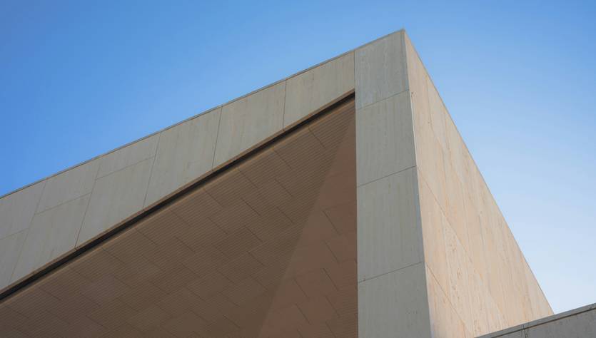 La imagen muestra un edificio moderno con líneas geométricas y un cielo despejado de fondo.