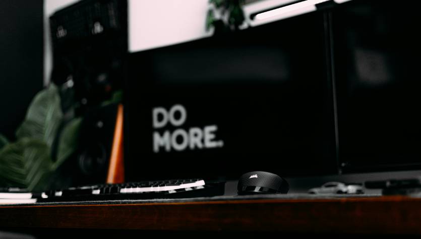 Una oficina minimalista con un teclado, un ratón y dos monitores donde se destaca la frase 'DO MORE.'