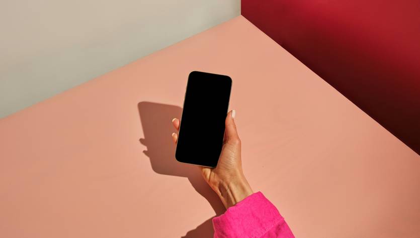 Una mano sostiene un teléfono móvil en un entorno minimalista de colores suaves.
