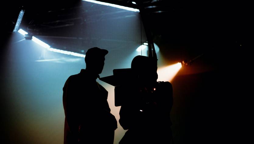 La imagen muestra la silueta de dos personas en un estudio de grabación con luces dramáticas de fondo.