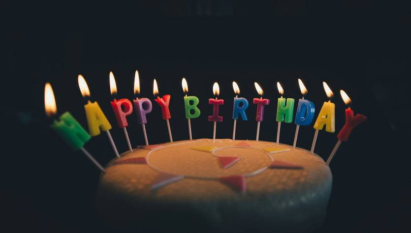 Un pastel de cumpleaños con velas de colores que forman la frase 'Feliz Cumpleaños'.
